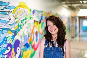 Becca-Borrelli-standing-in-front-of-Cunningham-Elementary-School-hand-painted-mural